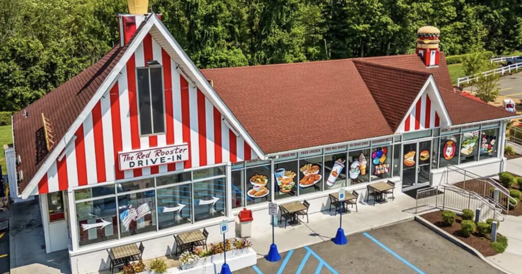 The Red Rooster Drive-In restaurant with custom painted vinyl window graphics showing burgers, fries, fried chicken, milkshakes, ice cream, and other menu items on the storefront windows.